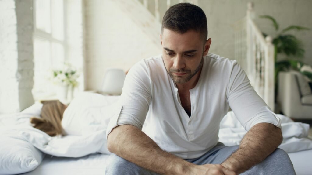 Pensive man sitting on bed in bright room