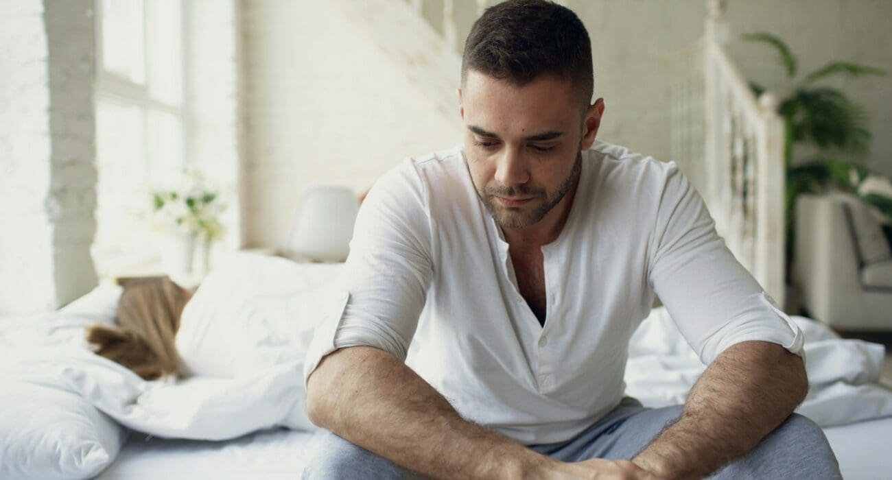 Pensive man sitting on bed in bright room