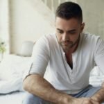 Pensive man sitting on bed in bright room